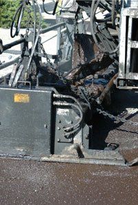 Asphalt paving machine dispensing hot, dark asphalt onto a road surface.