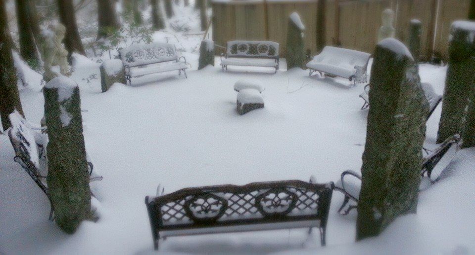 A ritual circle of benches and stones covered in snow with trees in the background.