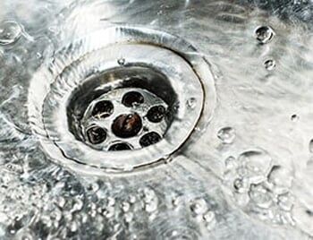 Stainless steel sink plug hole close up with water — Drain Cleaning in Coon Rapids, MN Stainless steel sink plug hole close up with water — Drain Cleaning in Coon Rapids, MN