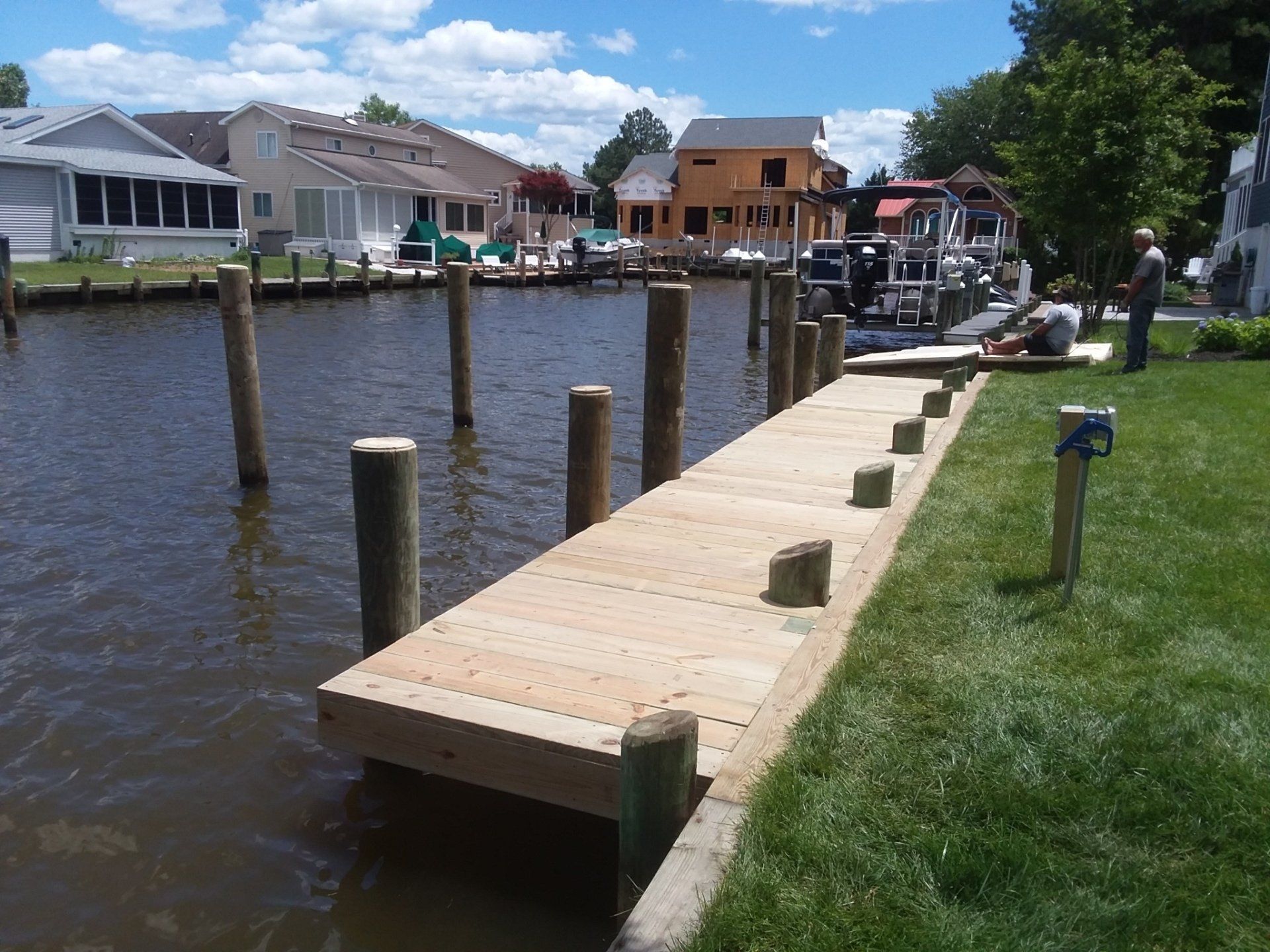 A newly constructed wooden dock extending into a canal, with pilings in the water and a house under construction nearby.