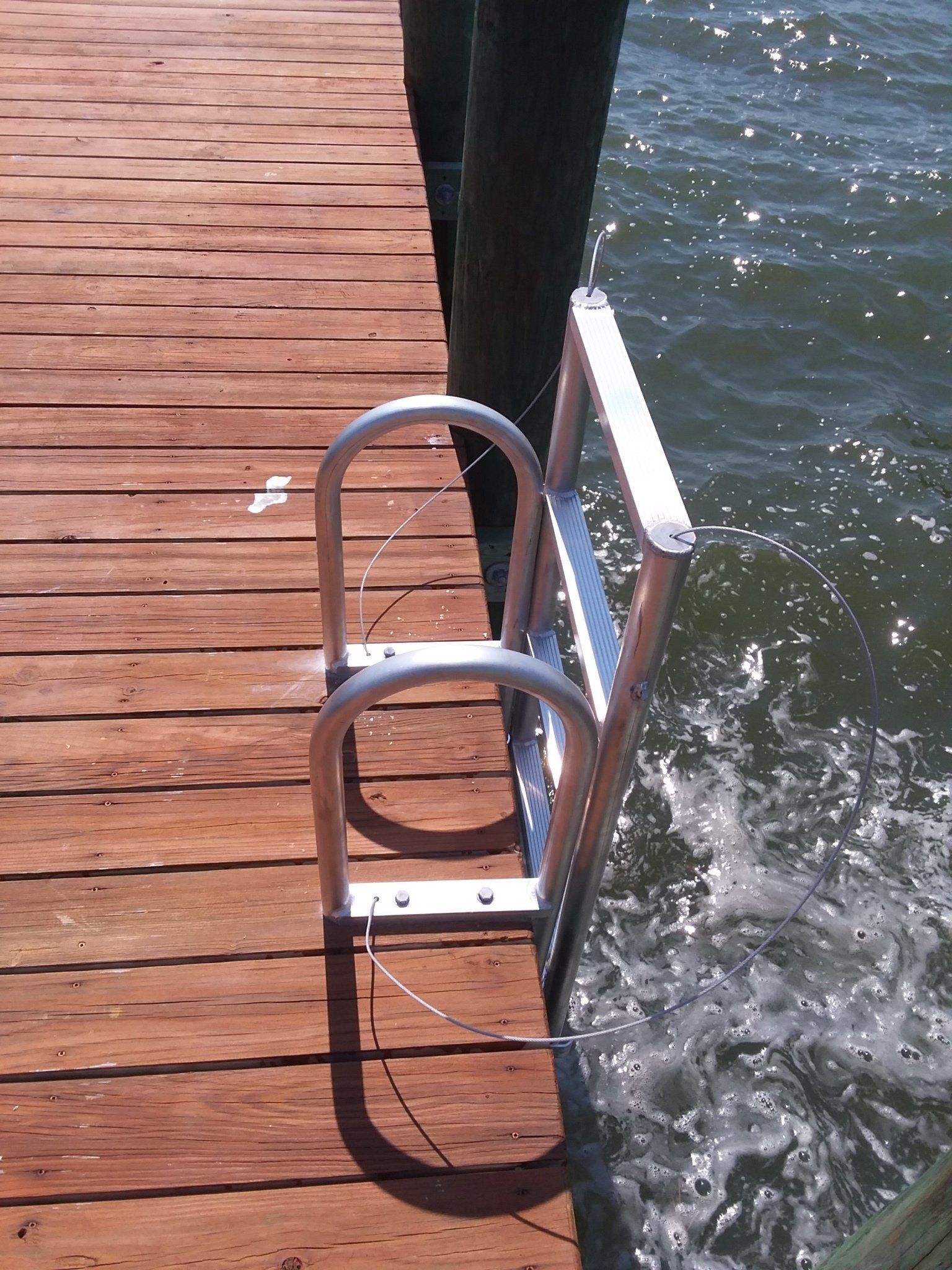 A metal dock ladder attached to the side of a wooden pier over splashing water.