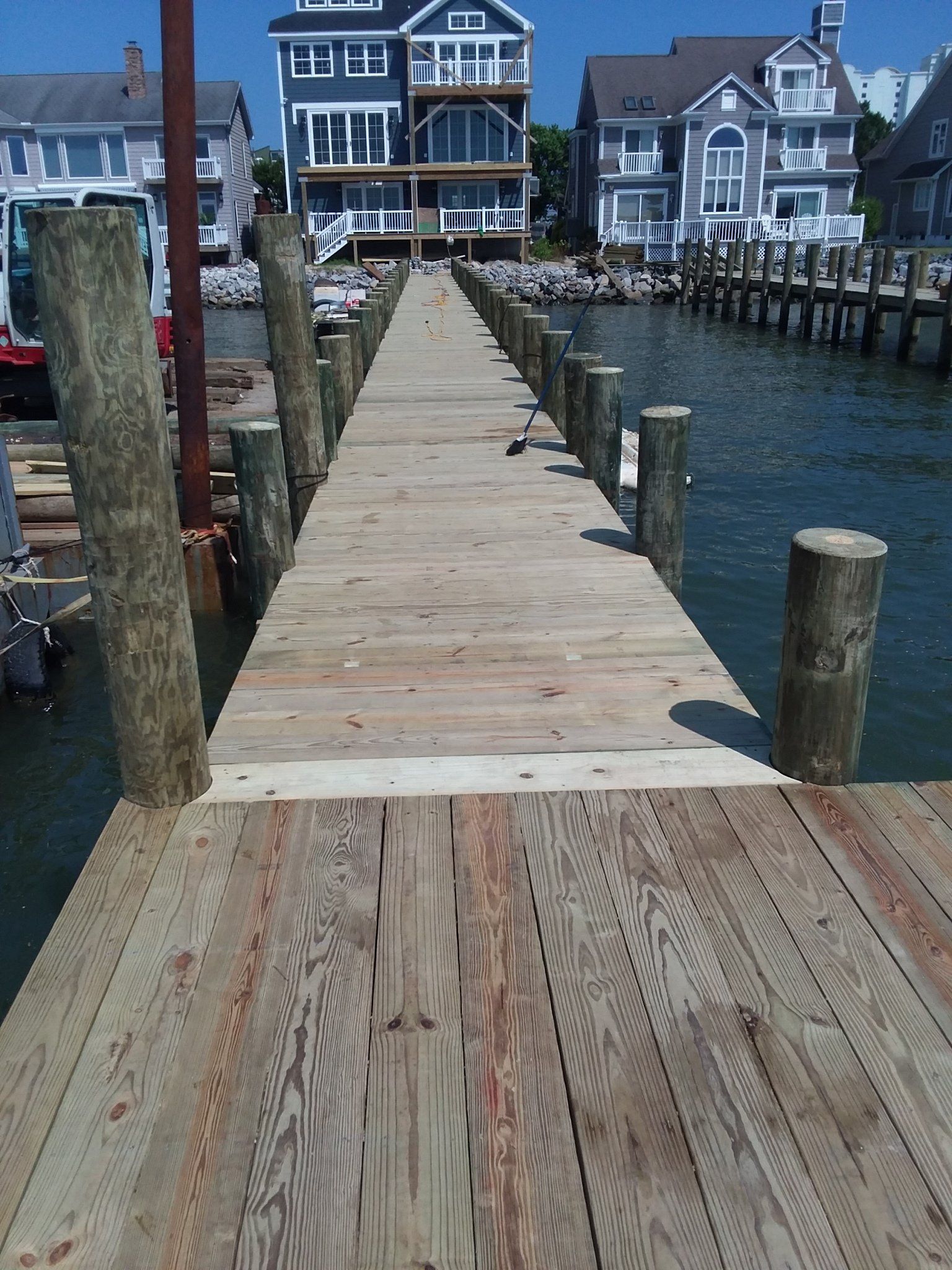 A wooden dock extends over water toward several multi-story houses on the shore.
