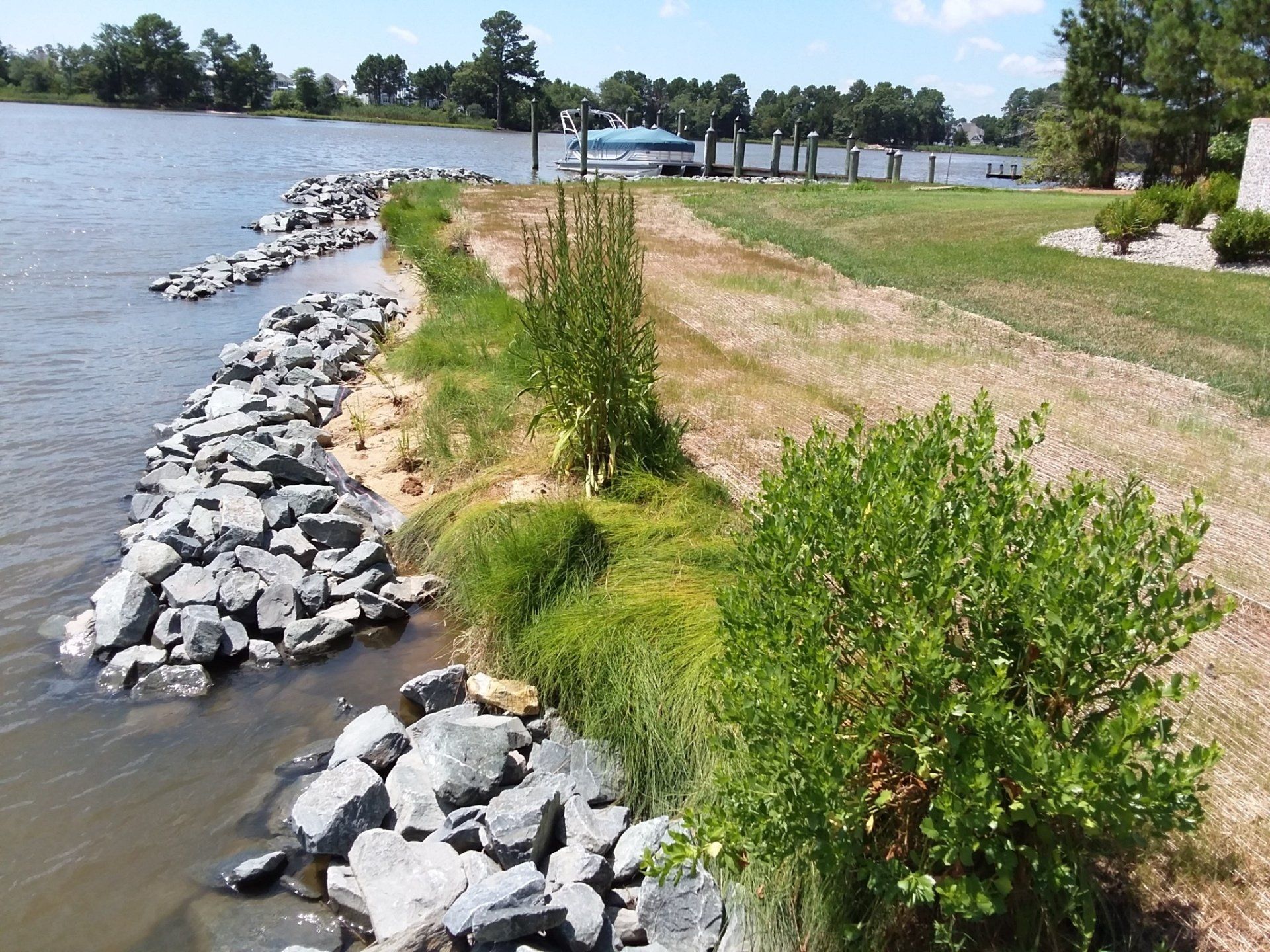 A riprap stone shoreline stabilization project bordering a grassy lawn and a blue body of water.