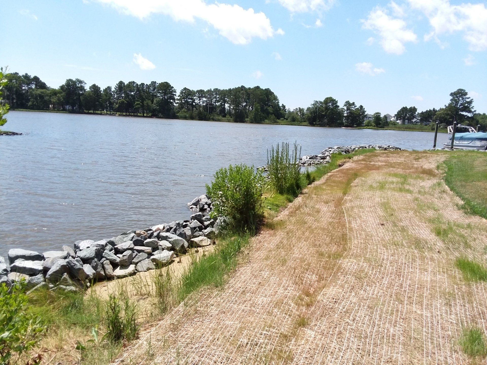 A body of water bordered by a rocky shoreline and a dry, grassy path under a blue sky with scattered clouds.