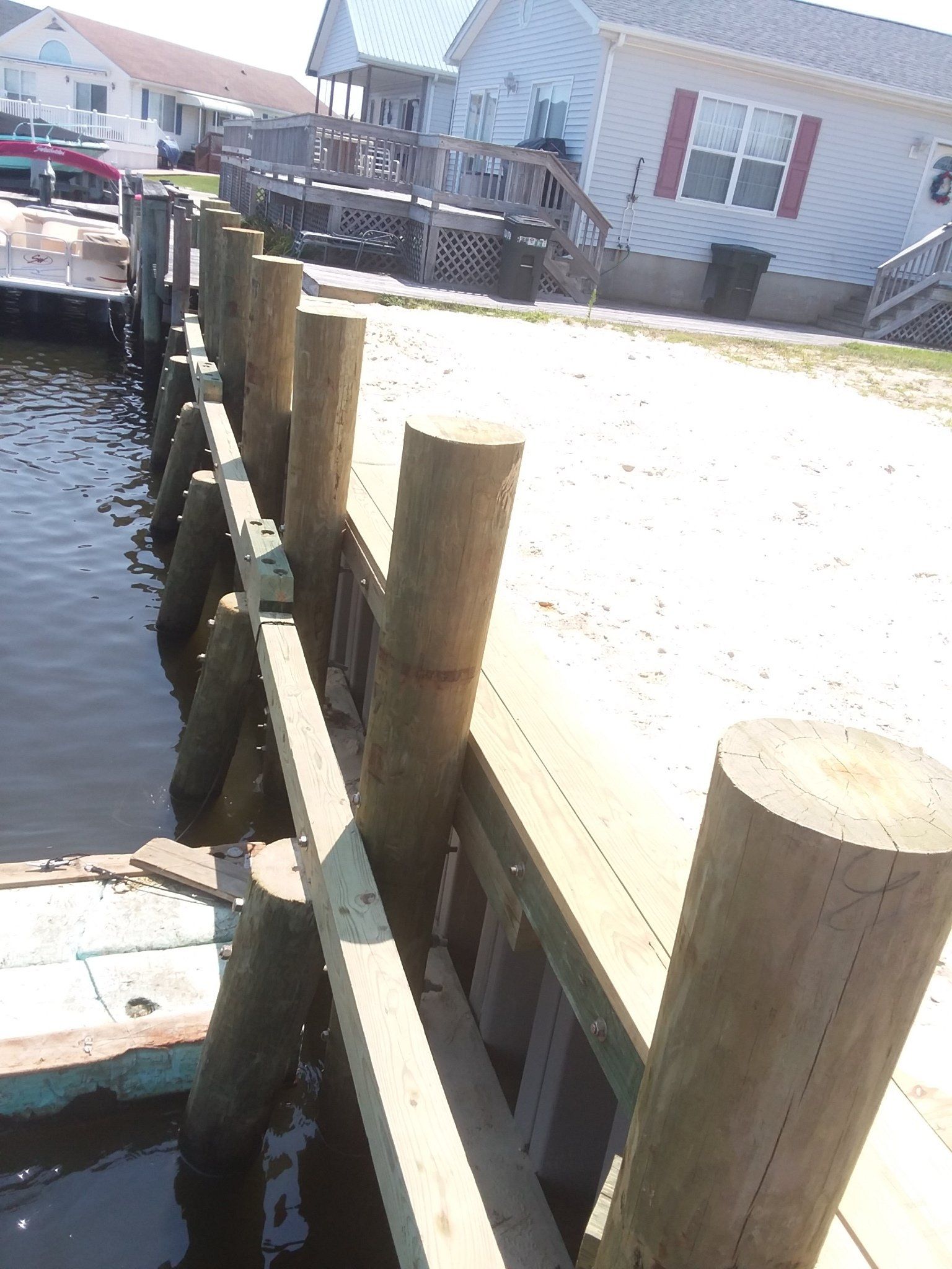 A wooden bulkhead with vertical pilings along a waterfront next to a residential house.