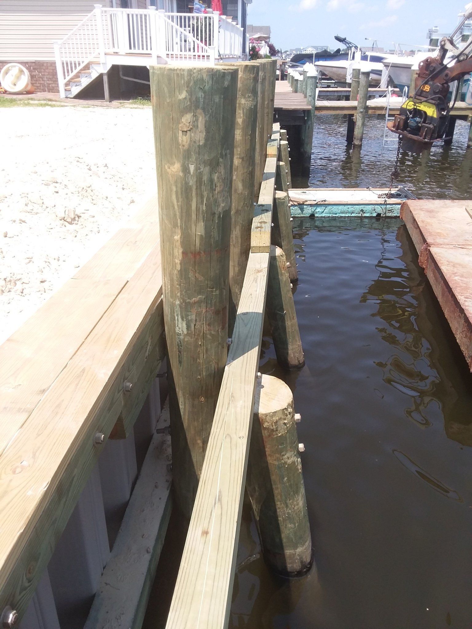 A view along a wooden dock showing vertical pilings secured to a bulkhead beside calm water and a floating boat dock.