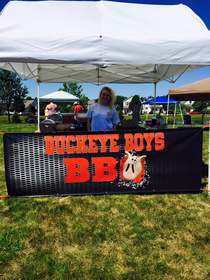 A woman stands behind a buckeye boys bbq sign