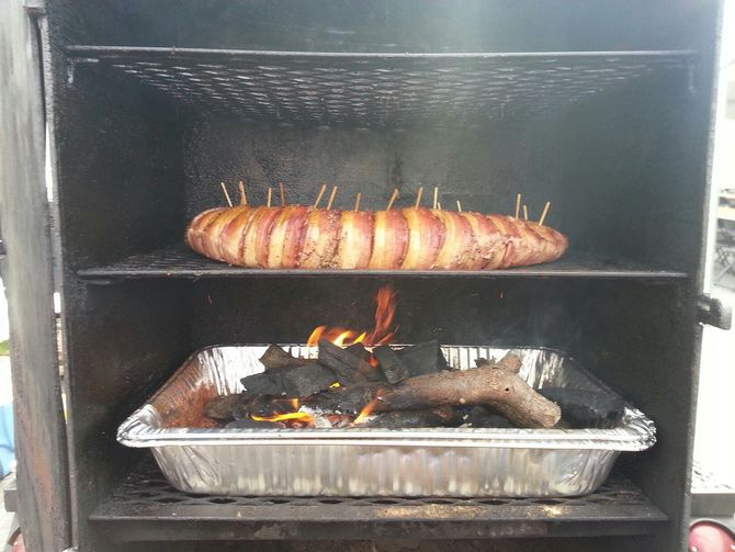 A bacon wrapped sausage is being cooked on a grill.