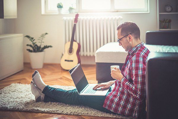 A man sitting on the ground on his laptop drinking coffee.