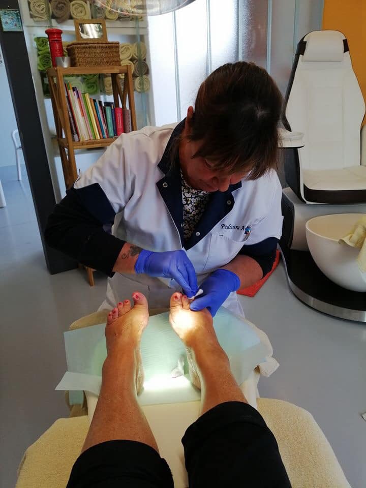 Een podotherapeut met blauwe handschoenen verzorgt de voet van een patiënt in een felverlichte behandelkamer.