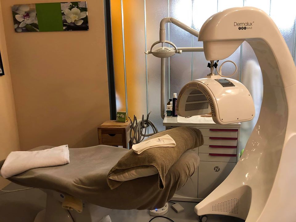 Behandelkamer met bed, lichttherapieapparaat en kast; lichtbeige muren.