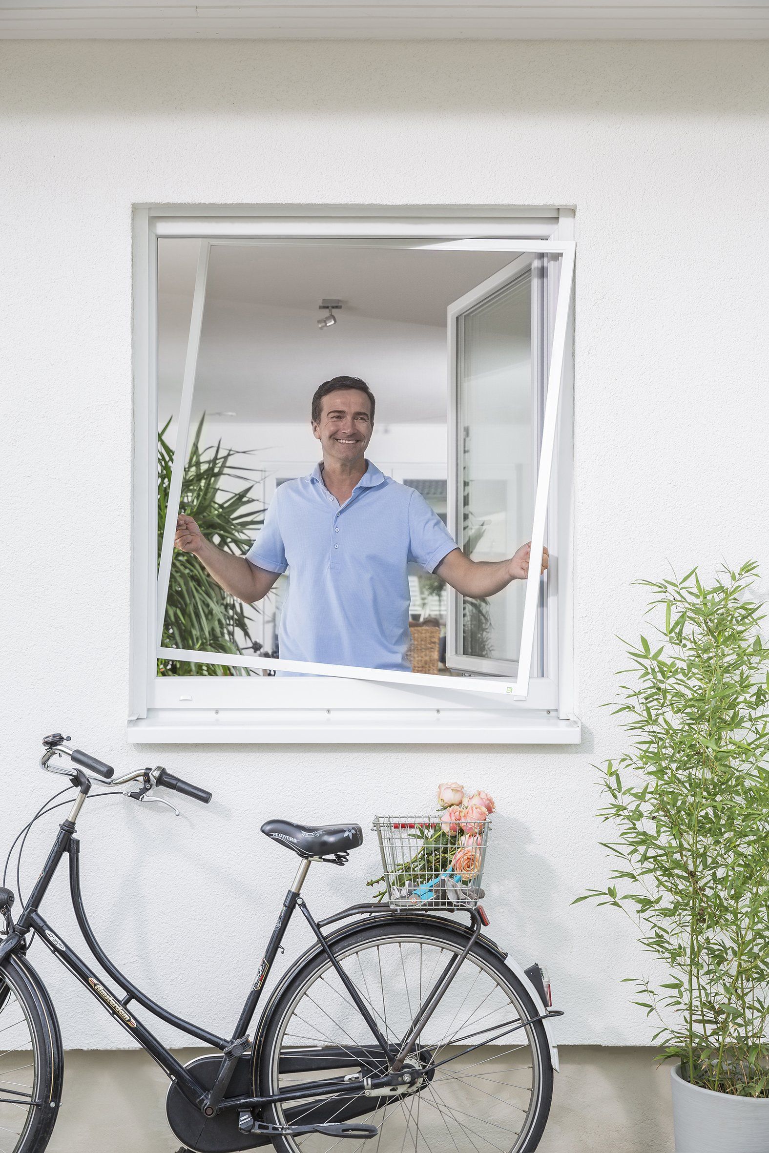 Mann steht in Küche und baut Insektenschutzgitter im Fenster ein