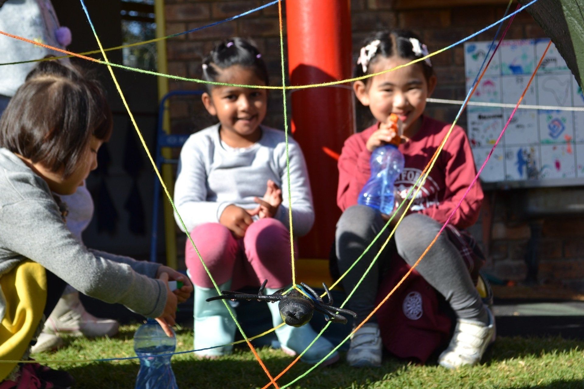 Three little girls are sitting on the grass playing with ropes.