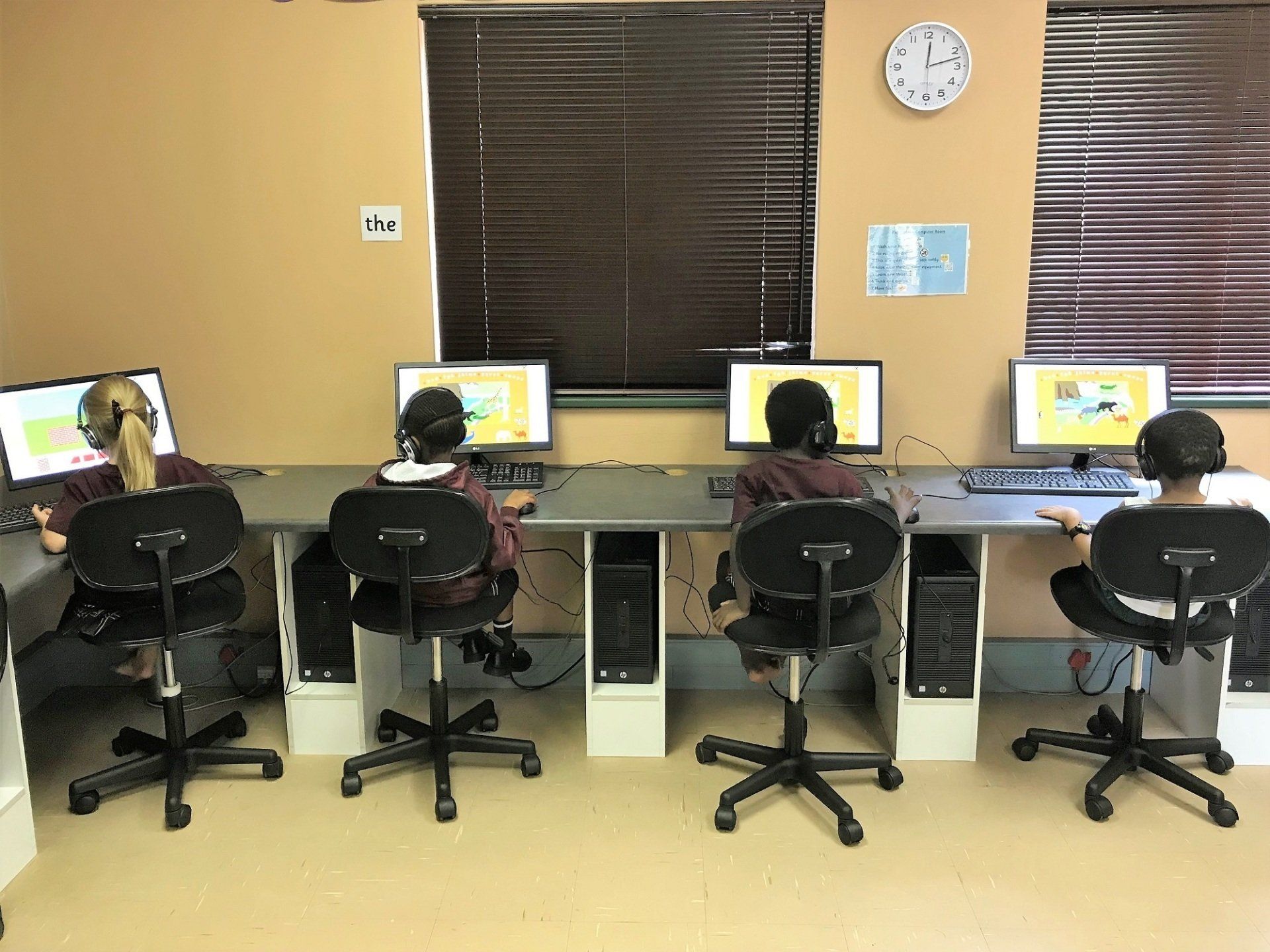 A group of people are sitting in front of computers in a room with a clock on the wall