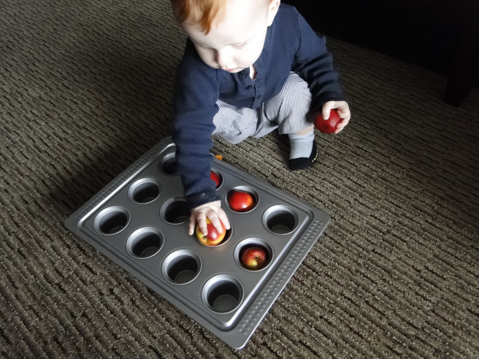A baby is playing with a muffin pan on the floor.