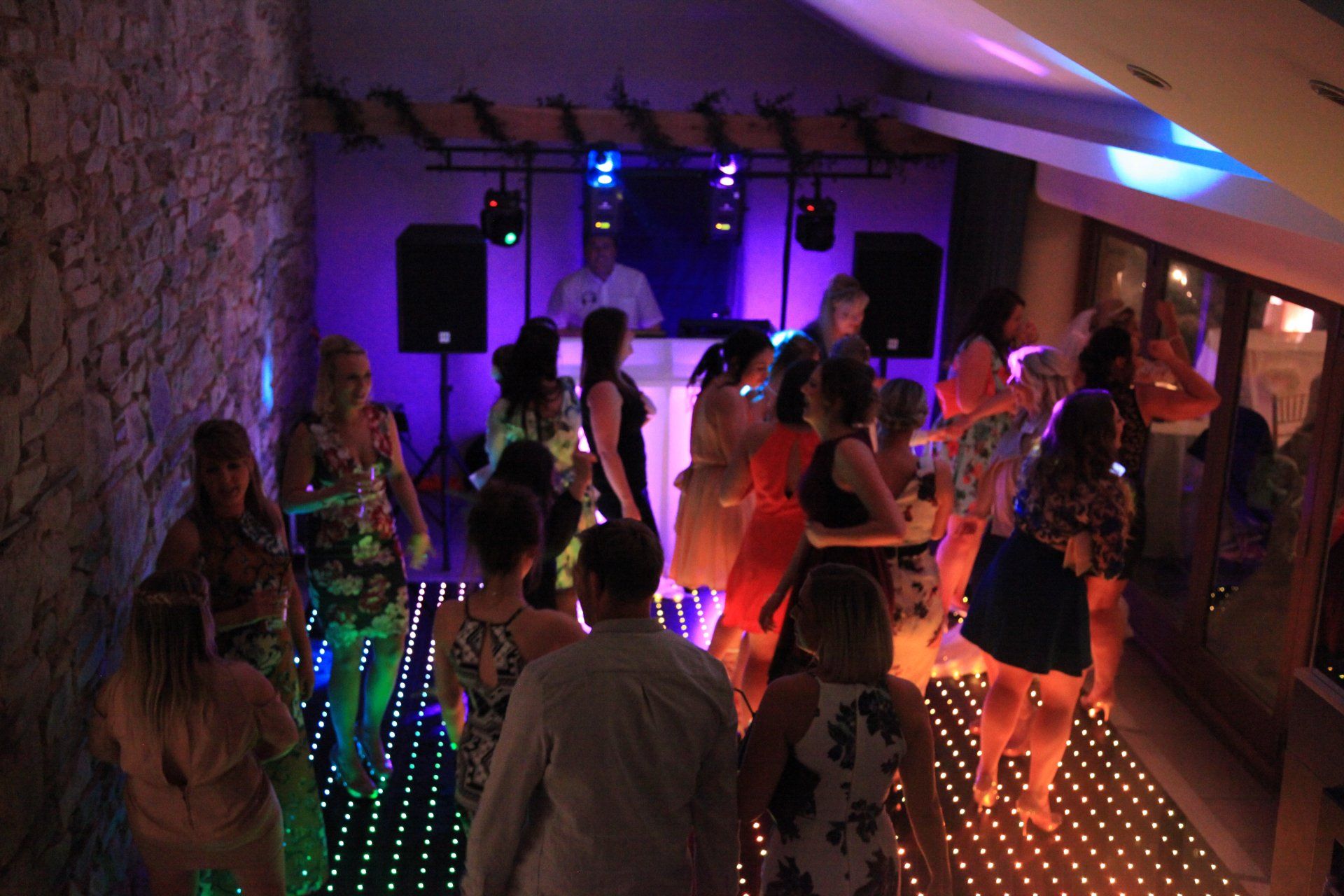 People dancing on a colorful dance floor, DJ booth in the background, dim lighting.
