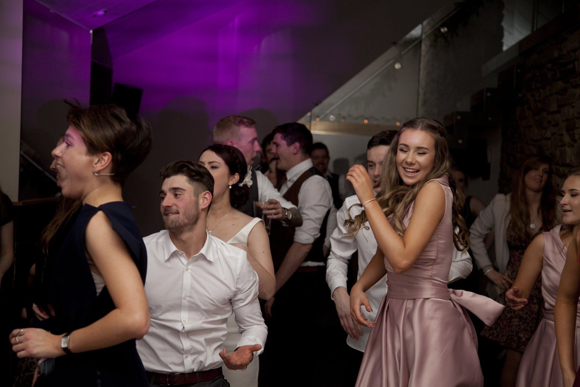 People dancing at a wedding reception, purple lighting, joyful expressions, and a bride and groom.