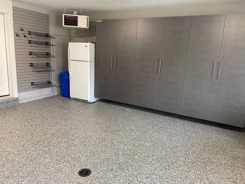 Long run of gray garage cabinets beside a fridge and slatwall on a flake floor