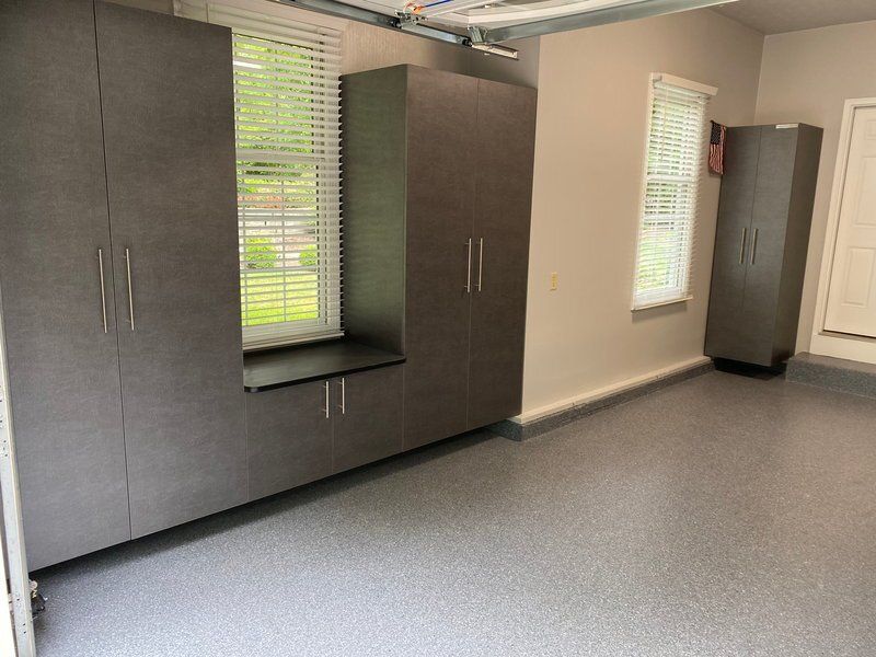 Dark gray garage cabinets framing a window on a light flake floor