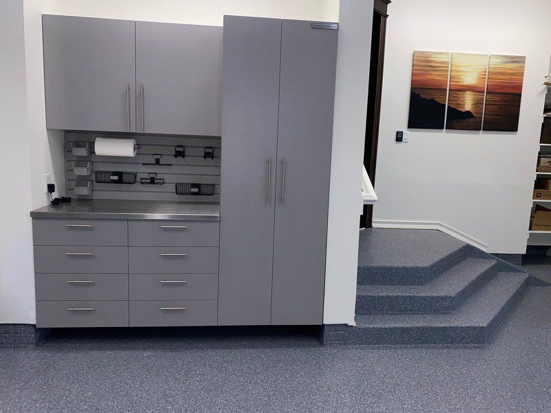 Gray garage cabinets with a stainless counter beside steps on a blue flake floor