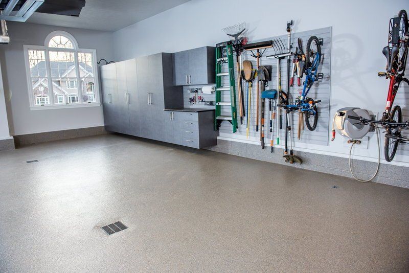 Gray garage cabinets and a slatwall with bikes and tools on a tan flake floor