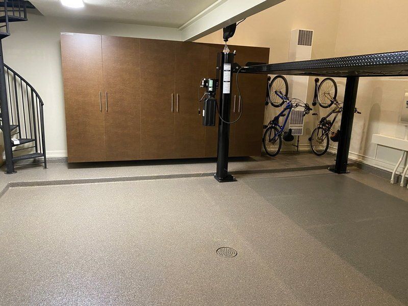 Bronze garage cabinets and a car lift on a gray flake floor with a border