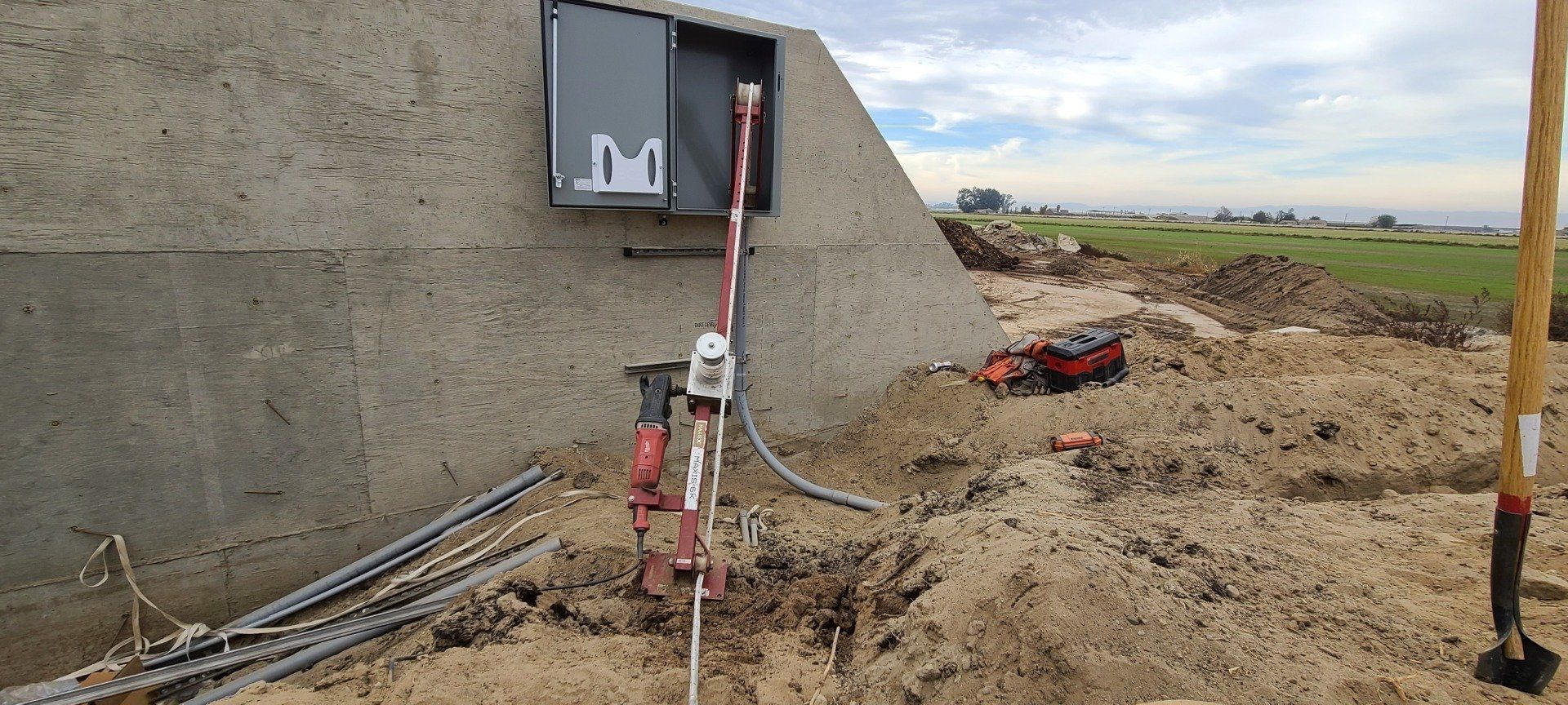 A box with the letter m on it is sitting in the dirt next to a shovel.