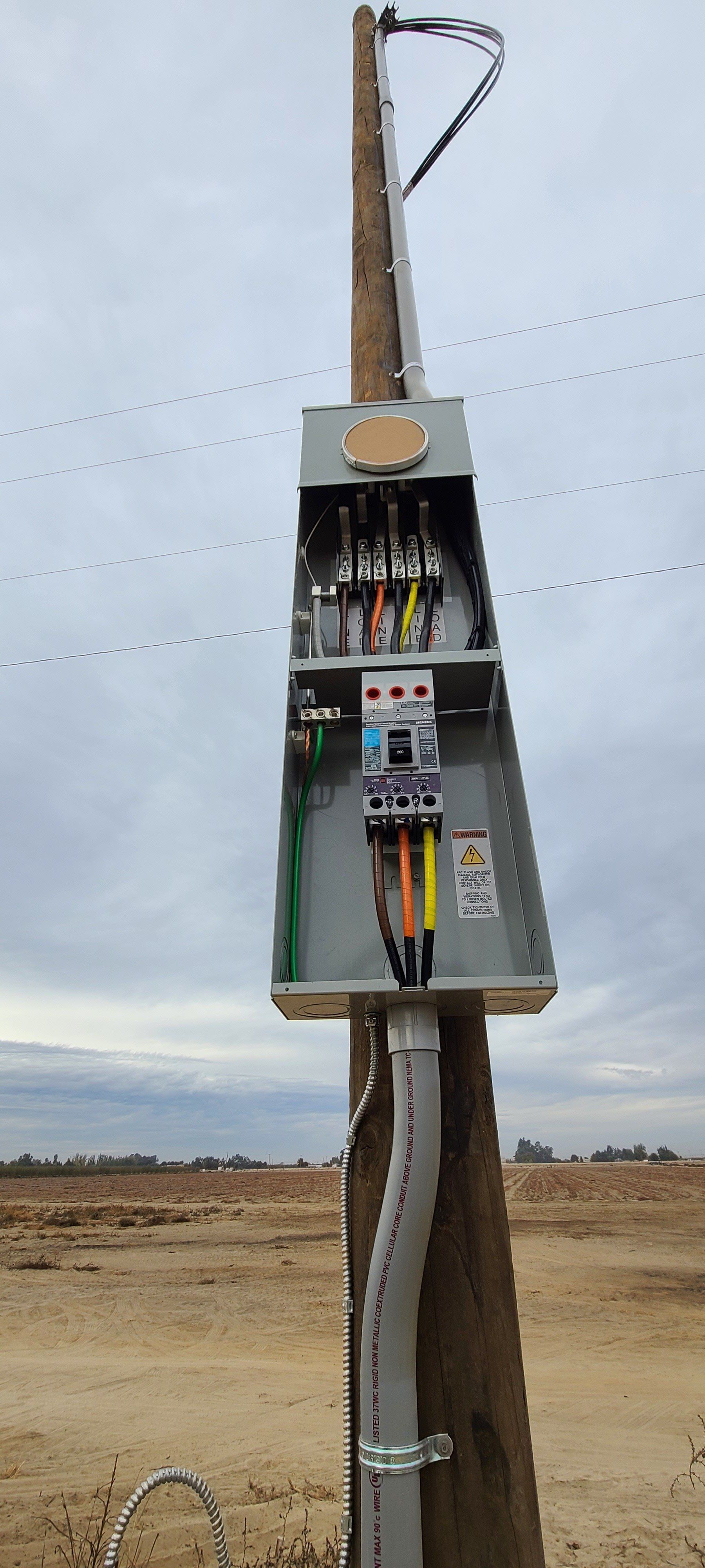 An electrical box is sitting on top of a wooden pole.