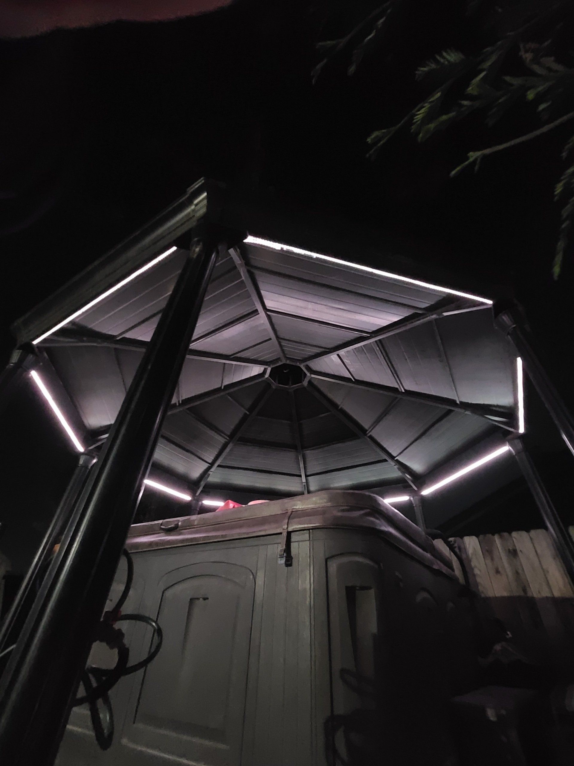 A gazebo with a hot tub underneath it is lit up at night.