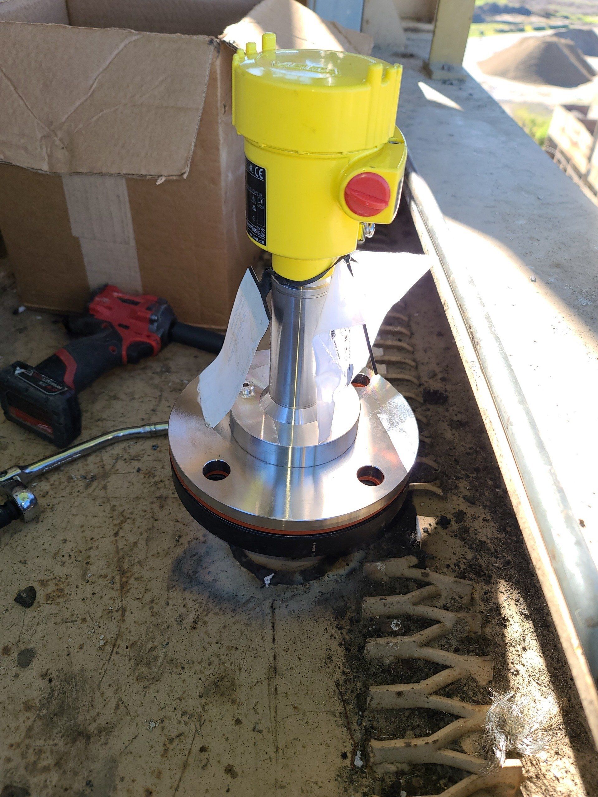 A yellow device is sitting on a table next to a box and a drill.