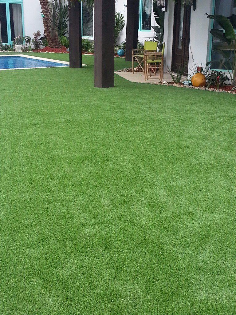 Green artificial turf yard with pool, patio furniture, and architectural columns.