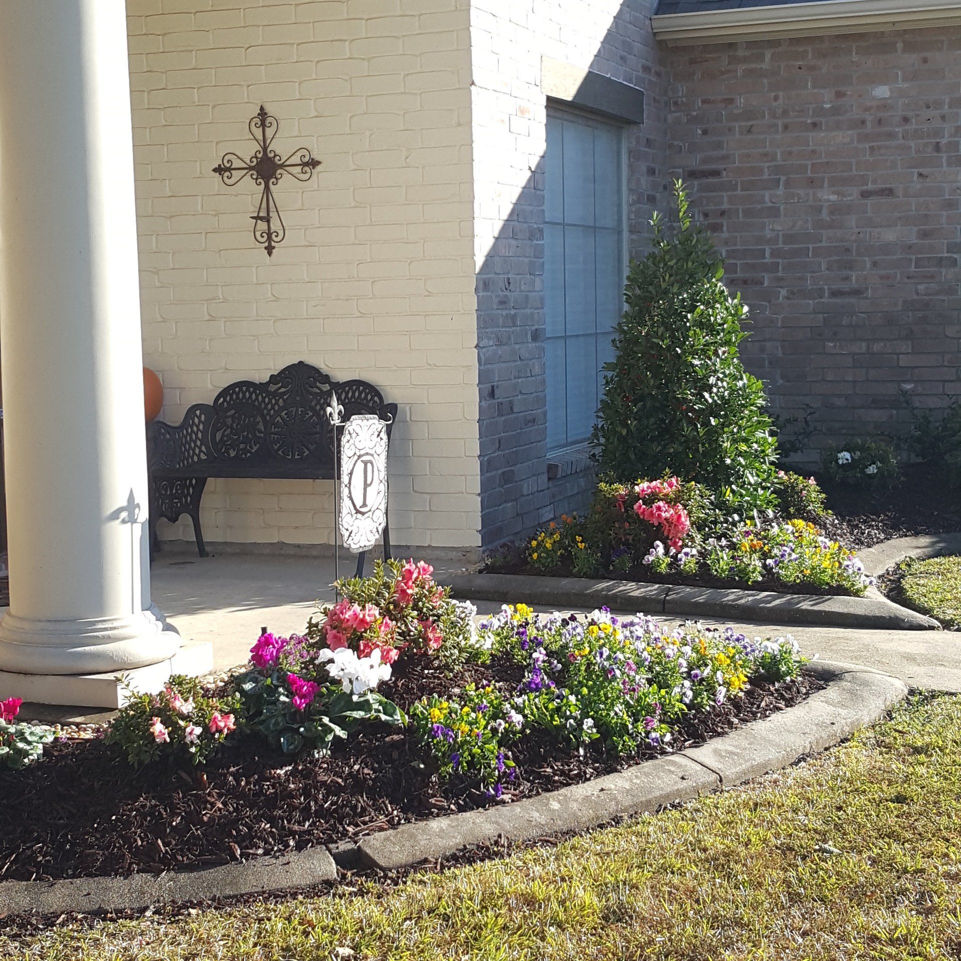 A house exterior with a garden bed full of colorful flowers and a black metal bench.