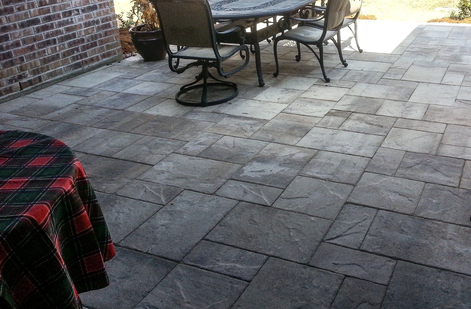 Patio with stone pavers, table and chairs. Tartan table cloth on the left, brick wall in the background.