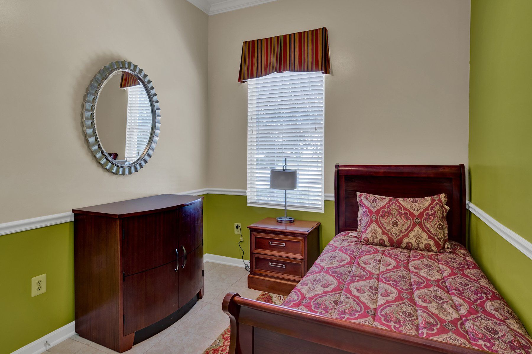 A bedroom with a bed , nightstand , mirror and window.