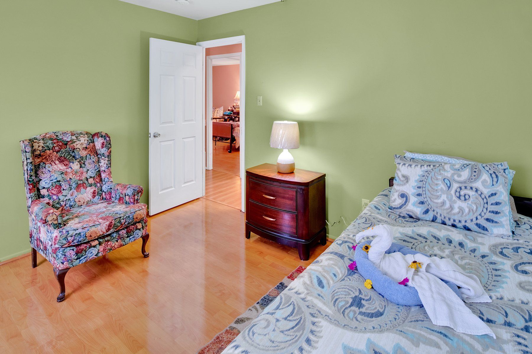 A bedroom with a bed , chair , nightstand and lamp.