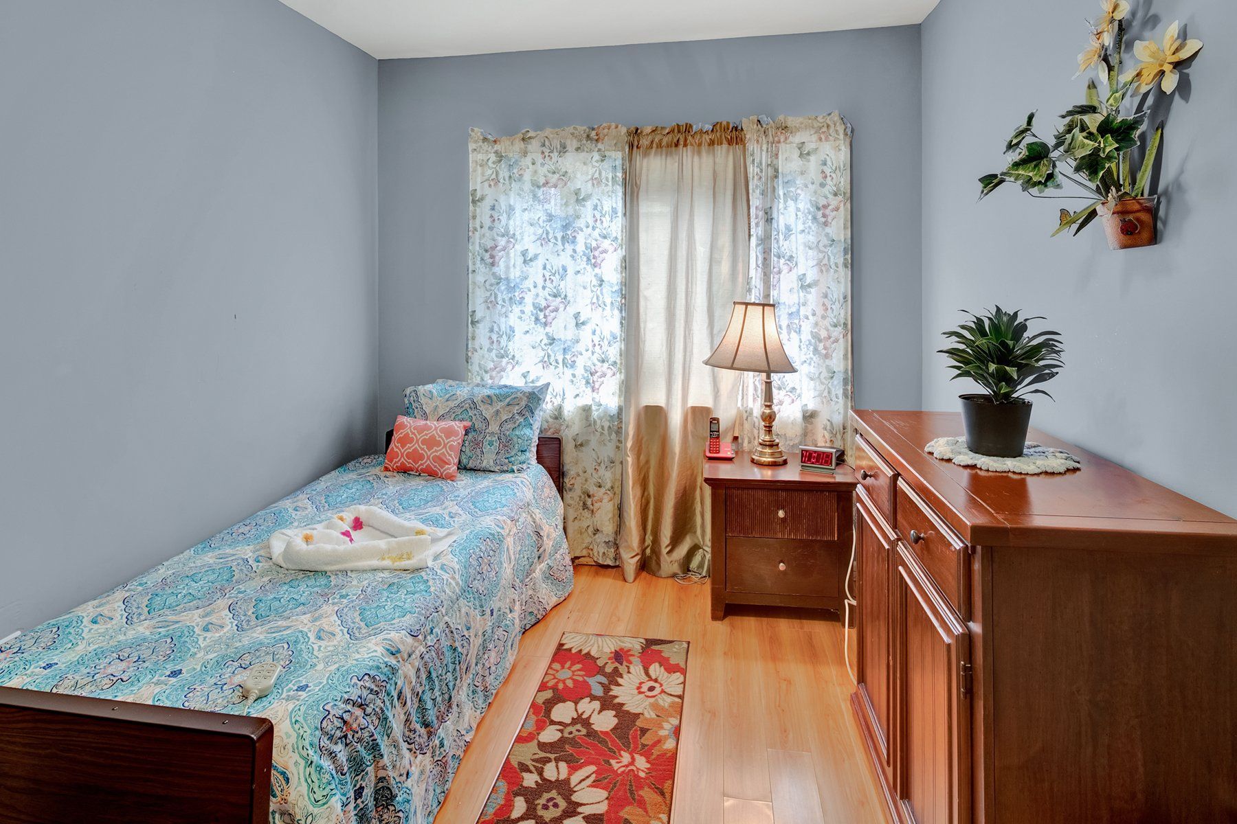 A bedroom with a single bed , nightstand , lamp and dresser.