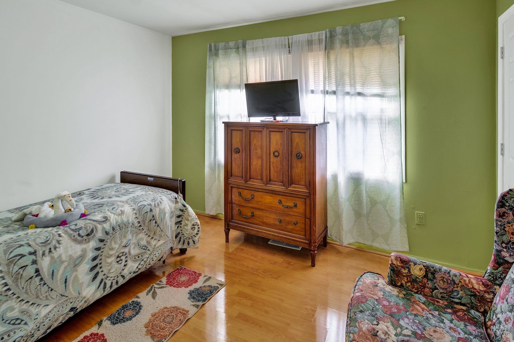 A bedroom with a bed , dresser , chair and television.