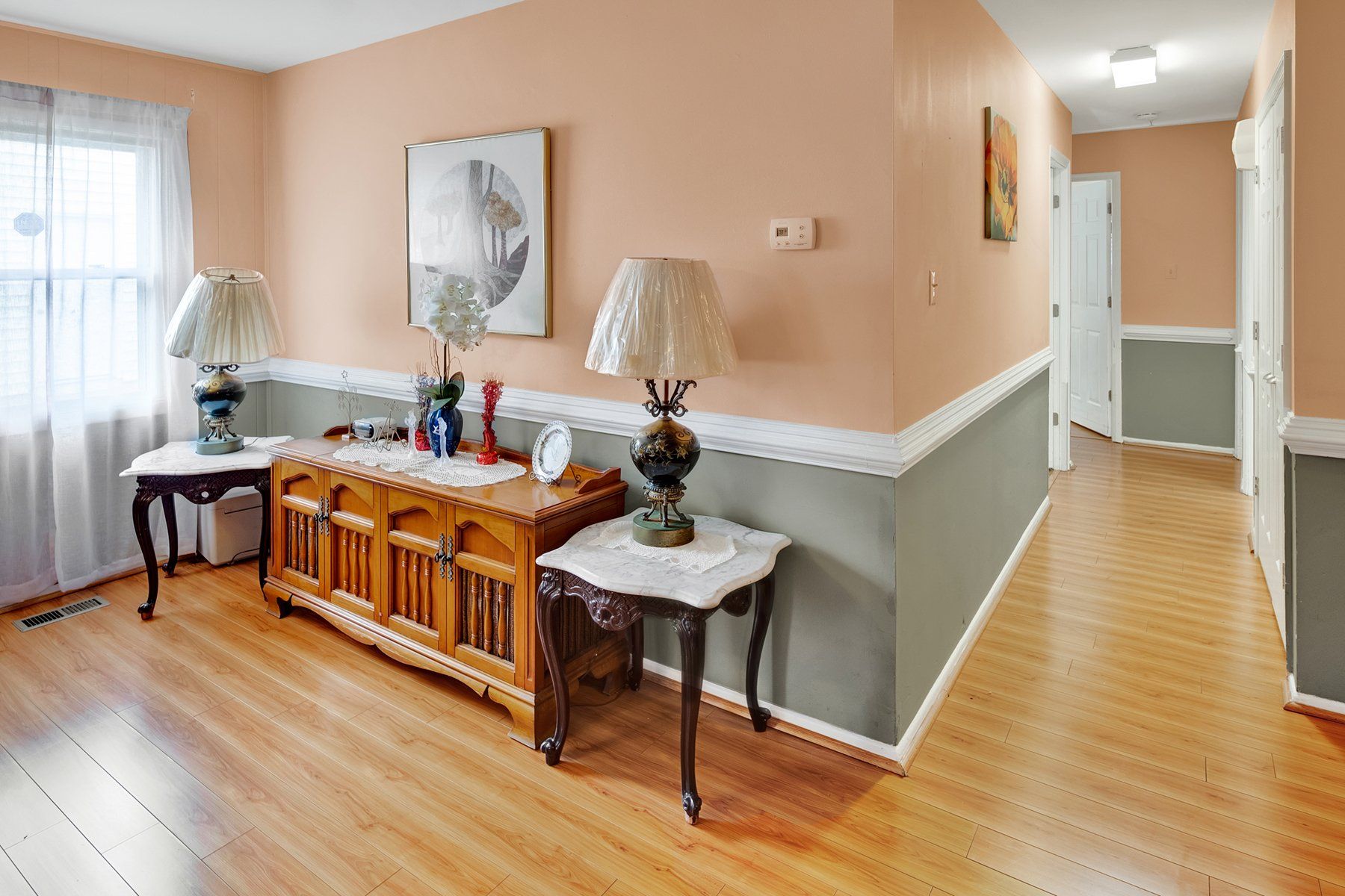 A hallway with hardwood floors , a dresser , lamps , and a picture on the wall.