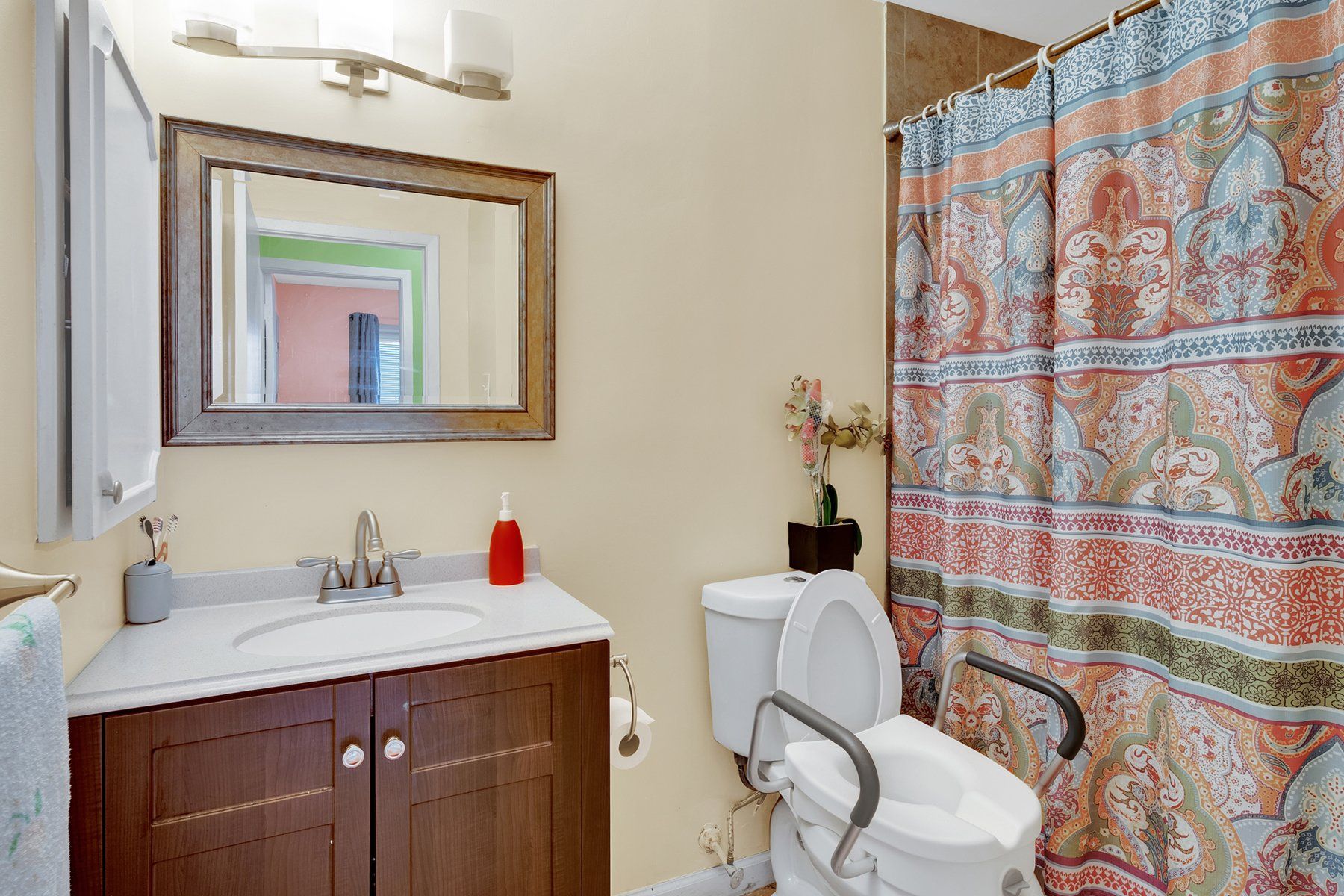 A bathroom with a toilet , sink , mirror and shower curtain.