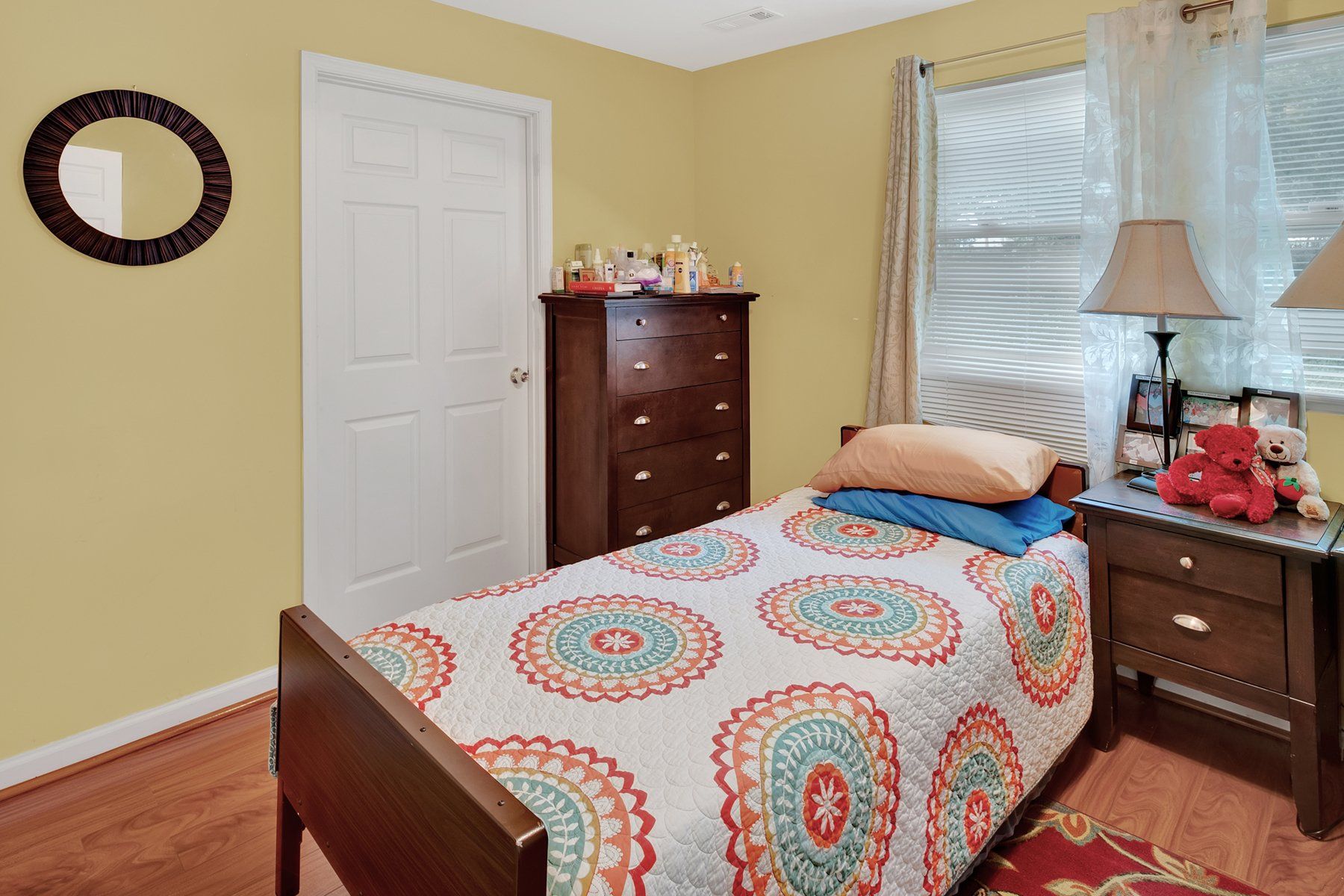 A bedroom with a single bed , dresser , nightstand and mirror.