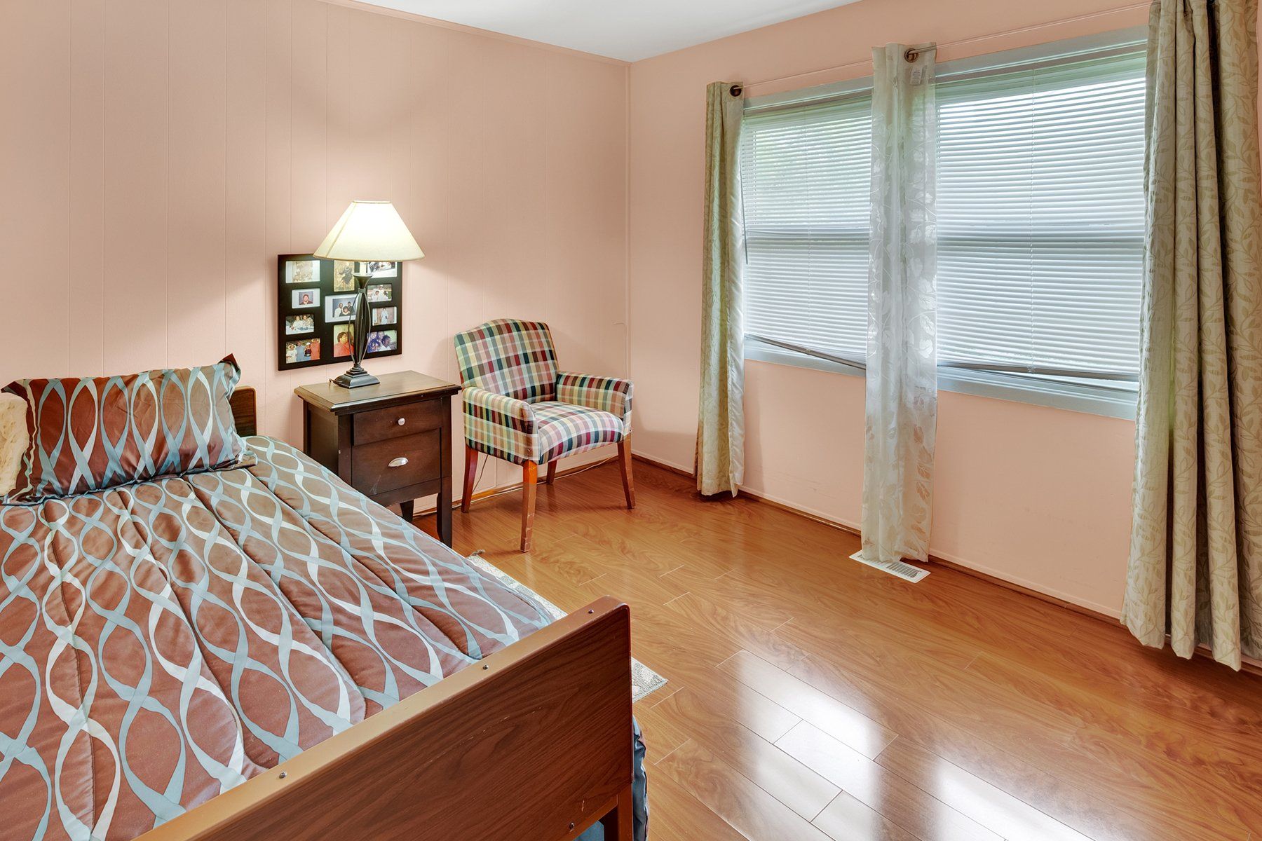 A bedroom with a bed , chair , nightstand and two windows.