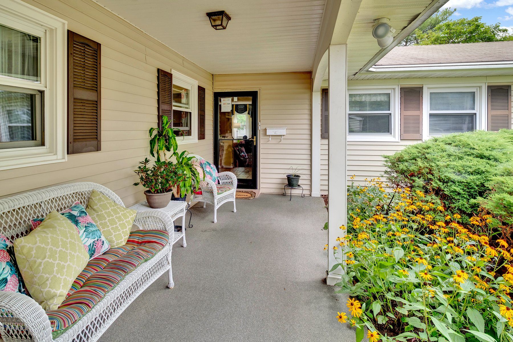 A porch with a wicker bench and chairs in front of a house.