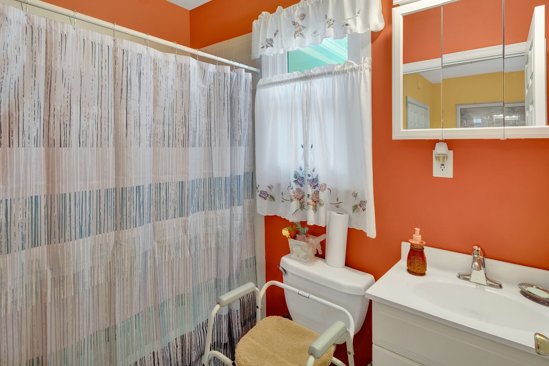 A bathroom with a toilet , sink , mirror and shower curtain.