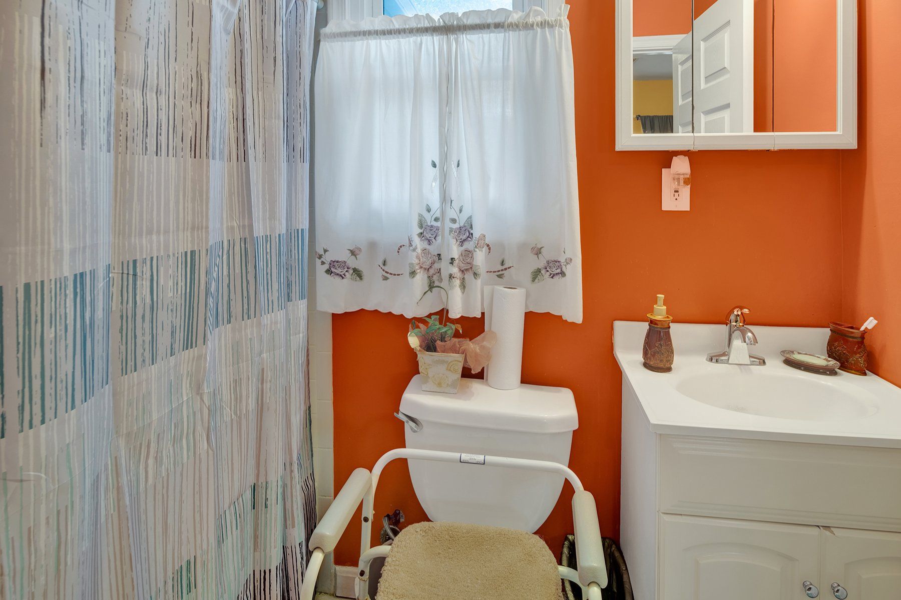 A bathroom with a toilet , sink , mirror and shower curtain.