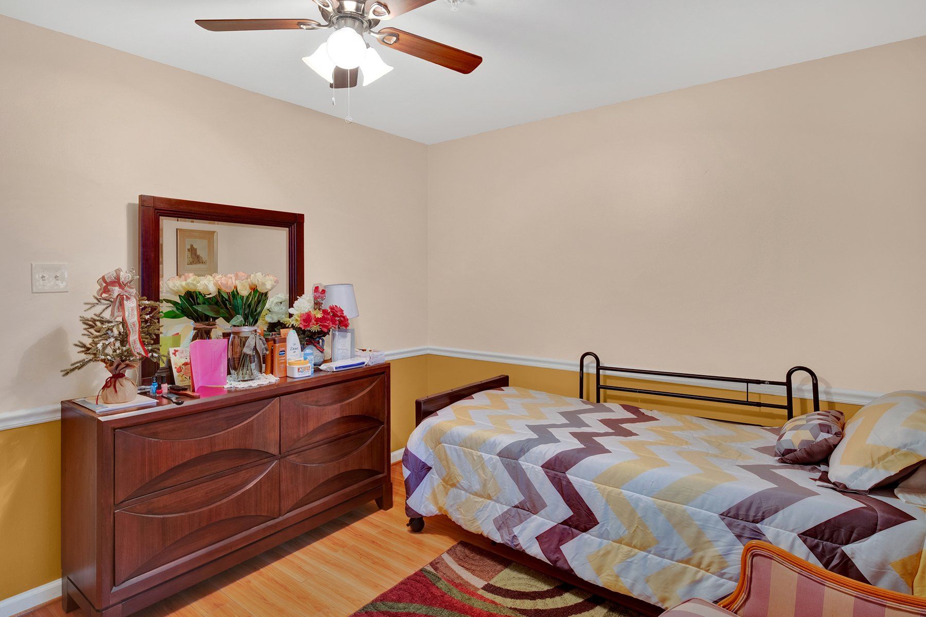 A bedroom with a bed , dresser , mirror and ceiling fan.