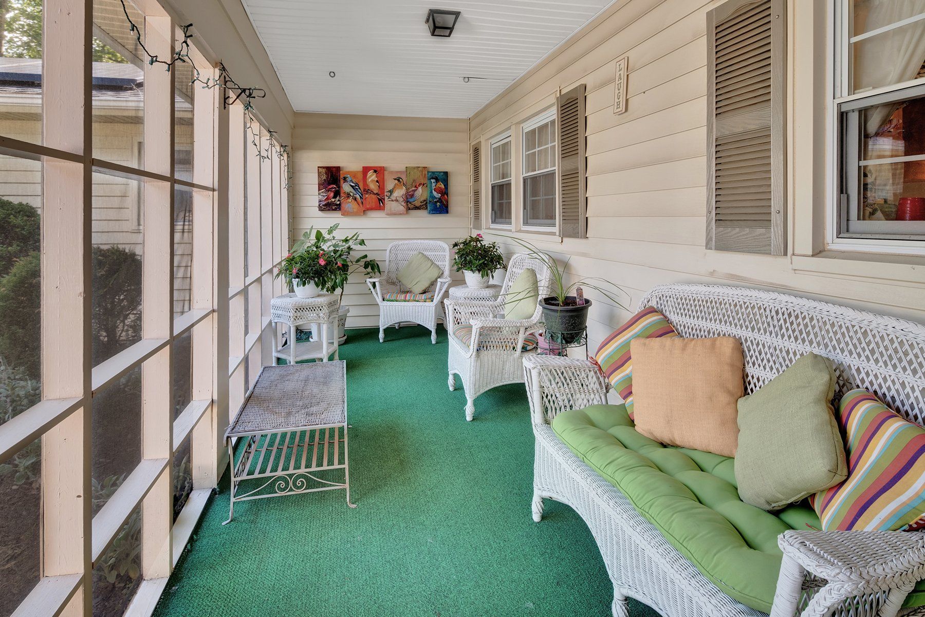 A screened in porch with a wicker bench and chairs.