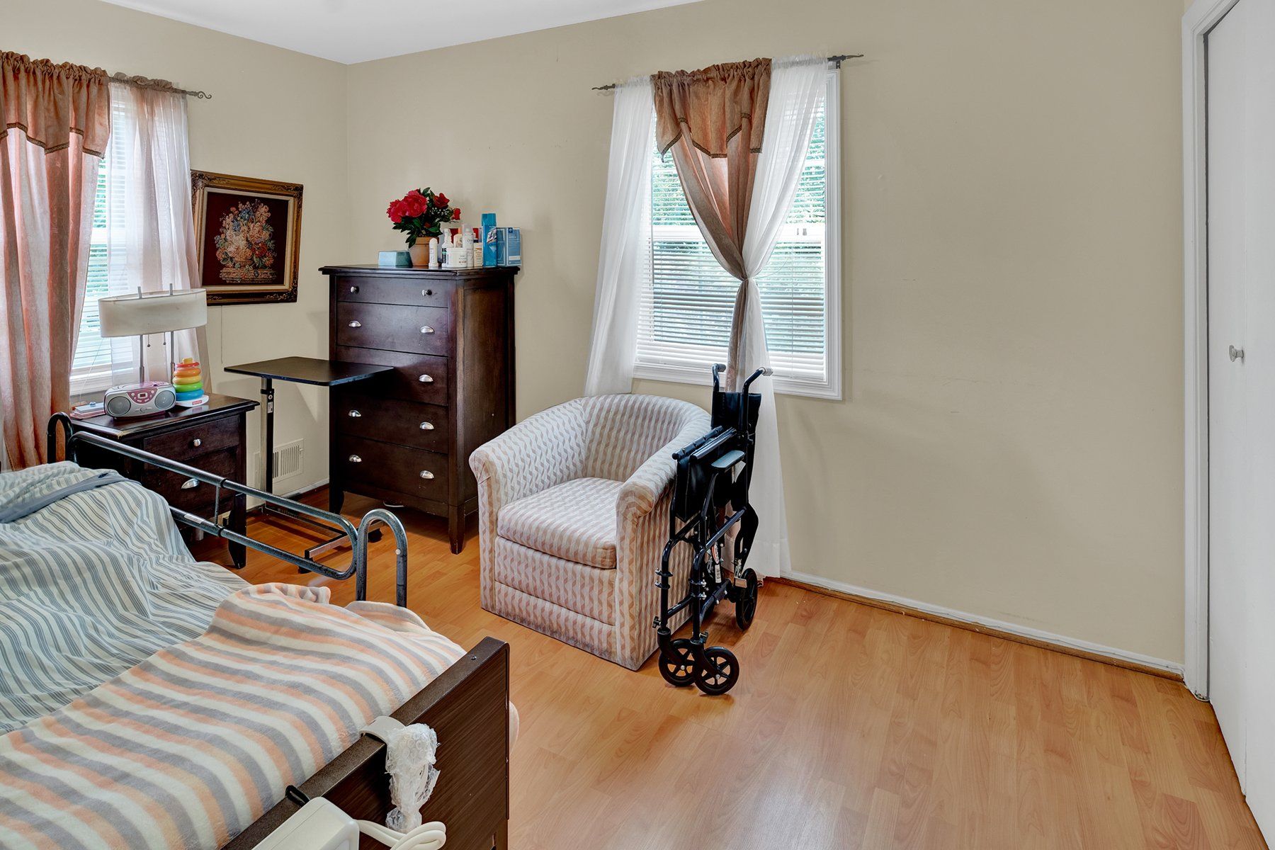 A bedroom with a bed , chair , dresser and wheelchair.