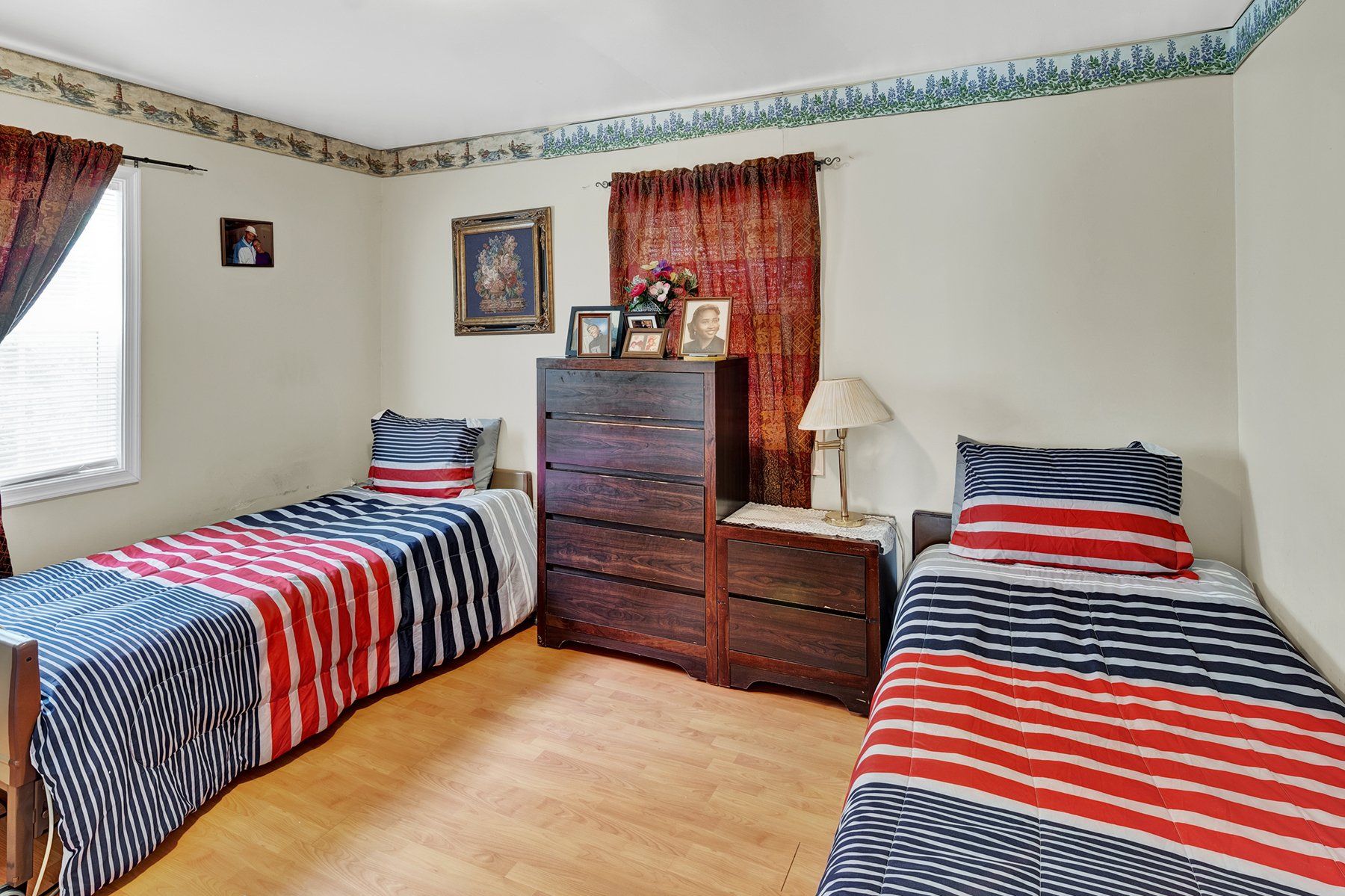 A bedroom with two beds , a dresser , and a lamp.
