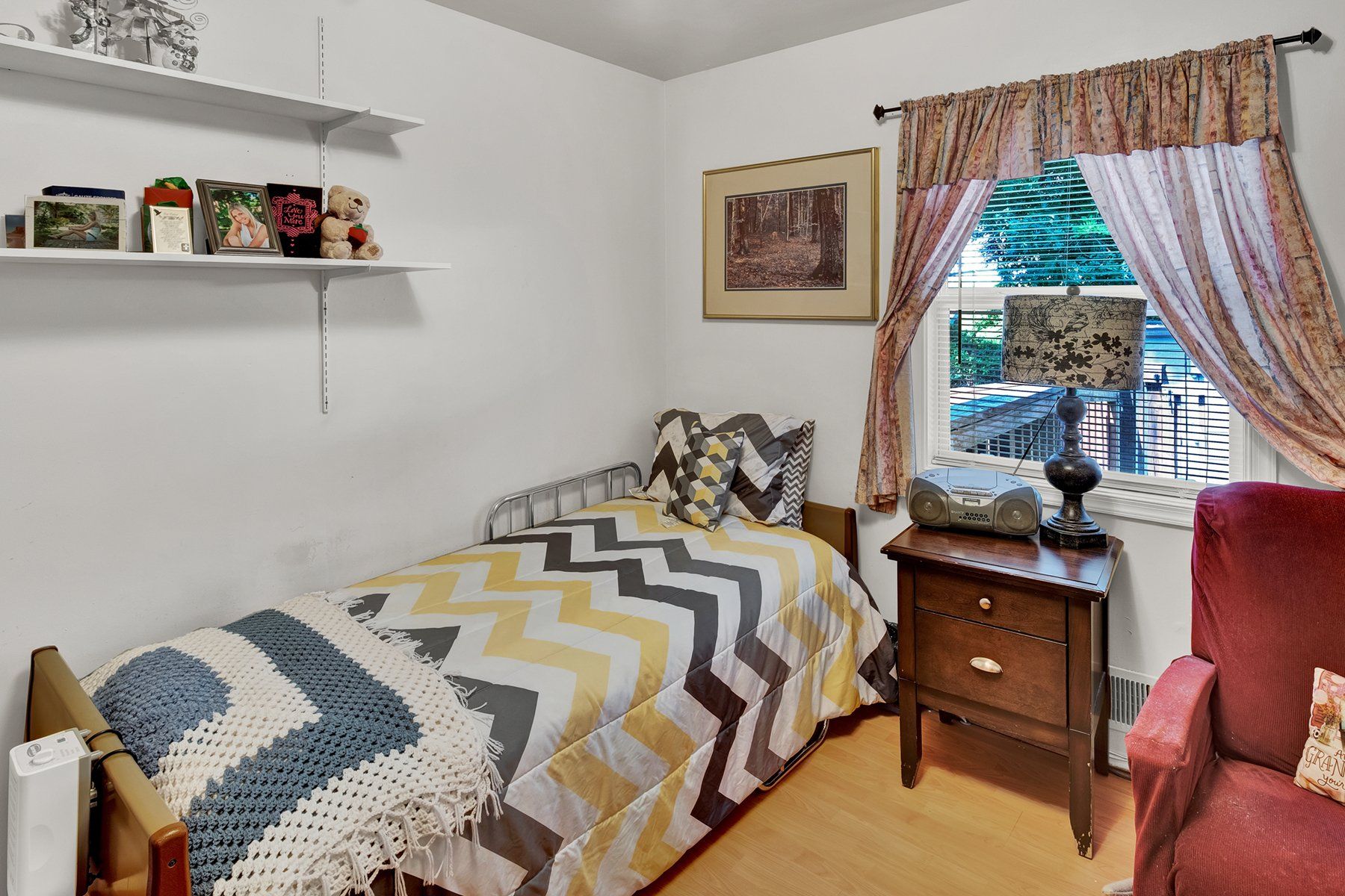 A bedroom with a single bed , nightstand , chair and window.