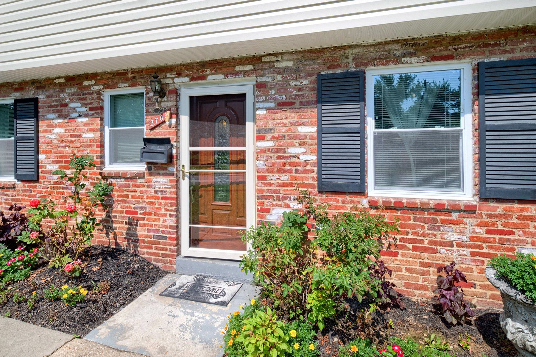 A brick house with a screen door and black shutters